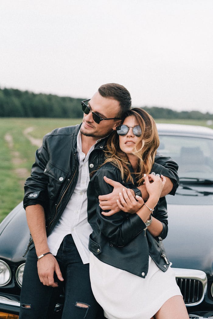 Charming couple in black leather jackets embracing by a car in the countryside.