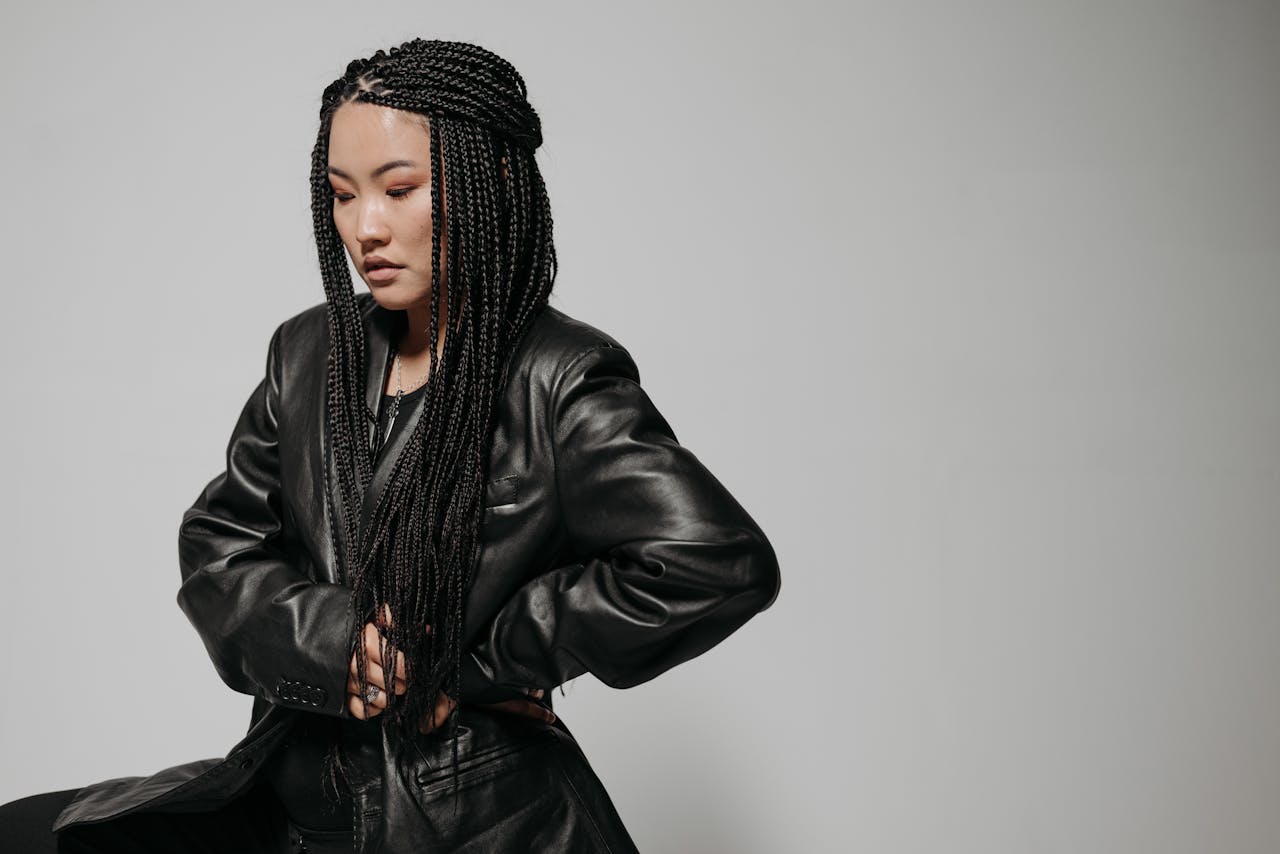 Fashionable woman with braided hair in a black leather jacket poses against a neutral background.